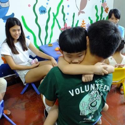 A Projects Abroad teenage volunteer working with children in China, holds a young child in the classroom. During teenage community volunteer work in China, a high school student hugs a young child in the classroom.